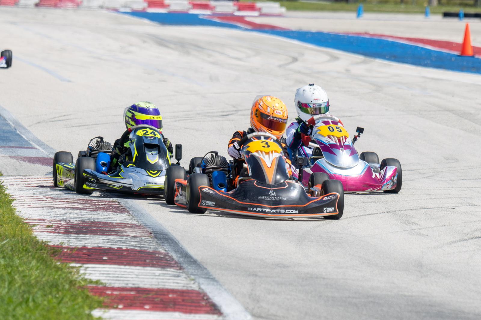 Three go-karts racing on a track with drivers wearing helmets.